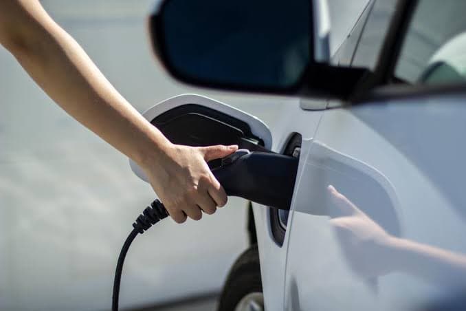Mão conectando o plugue de recarga na lateral de um carro elétrico.